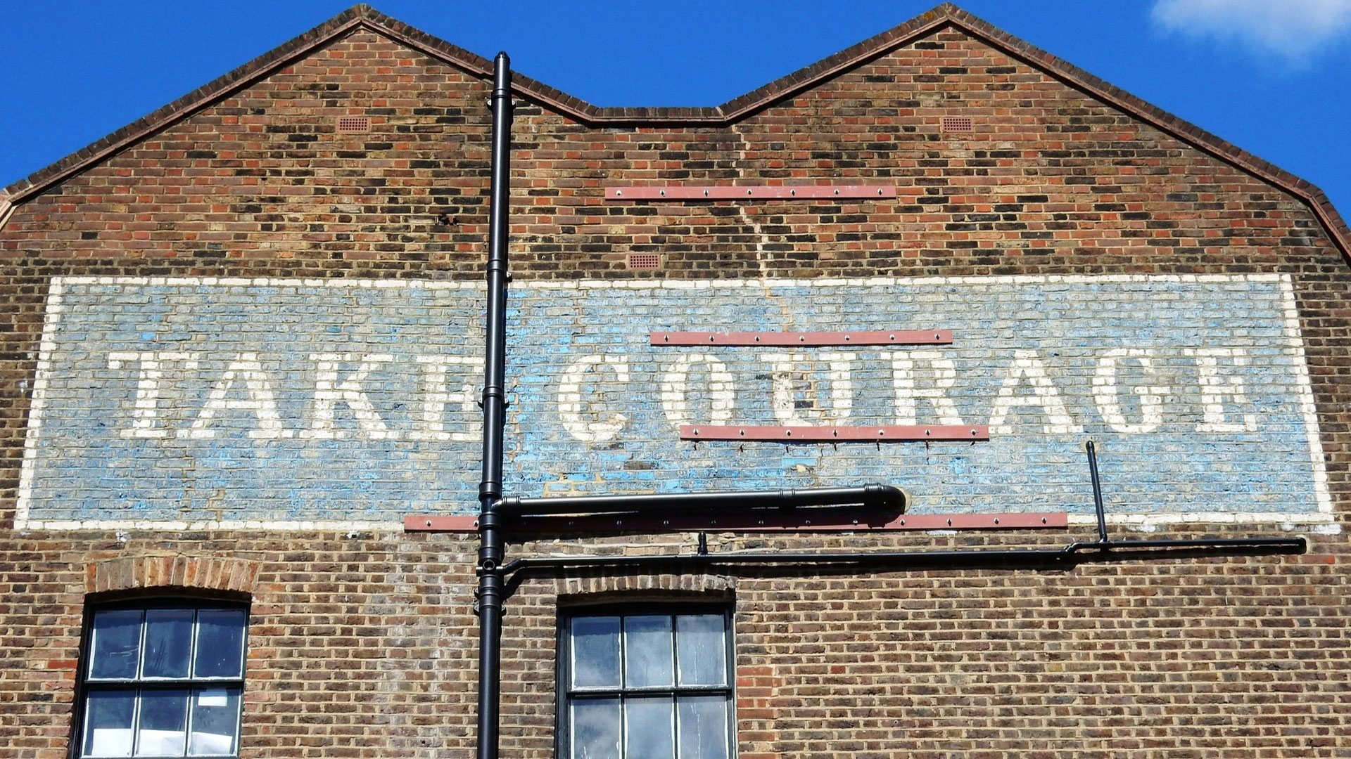 A faded advert, or ghost sign, saying Take Courage, painted onto a brick building