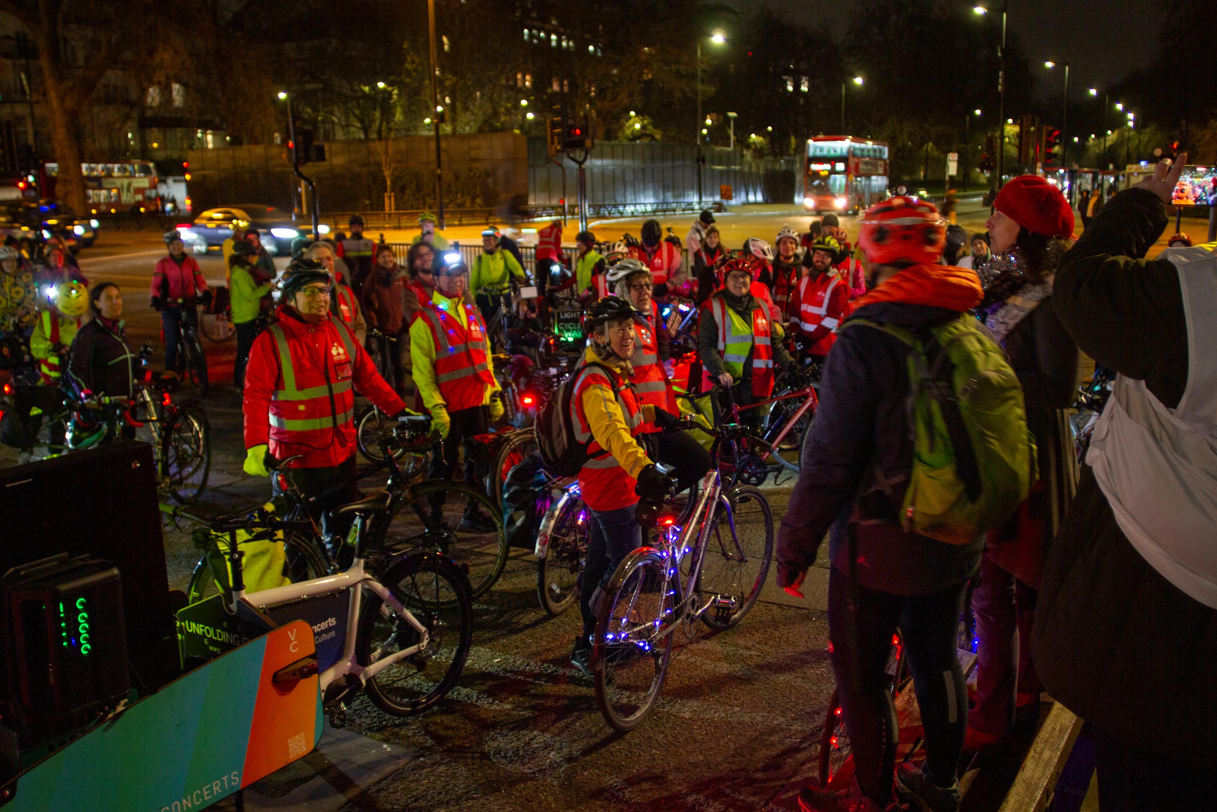 A group of about 50 cyclists standing with their bikes at night, at Marble Arch in London.