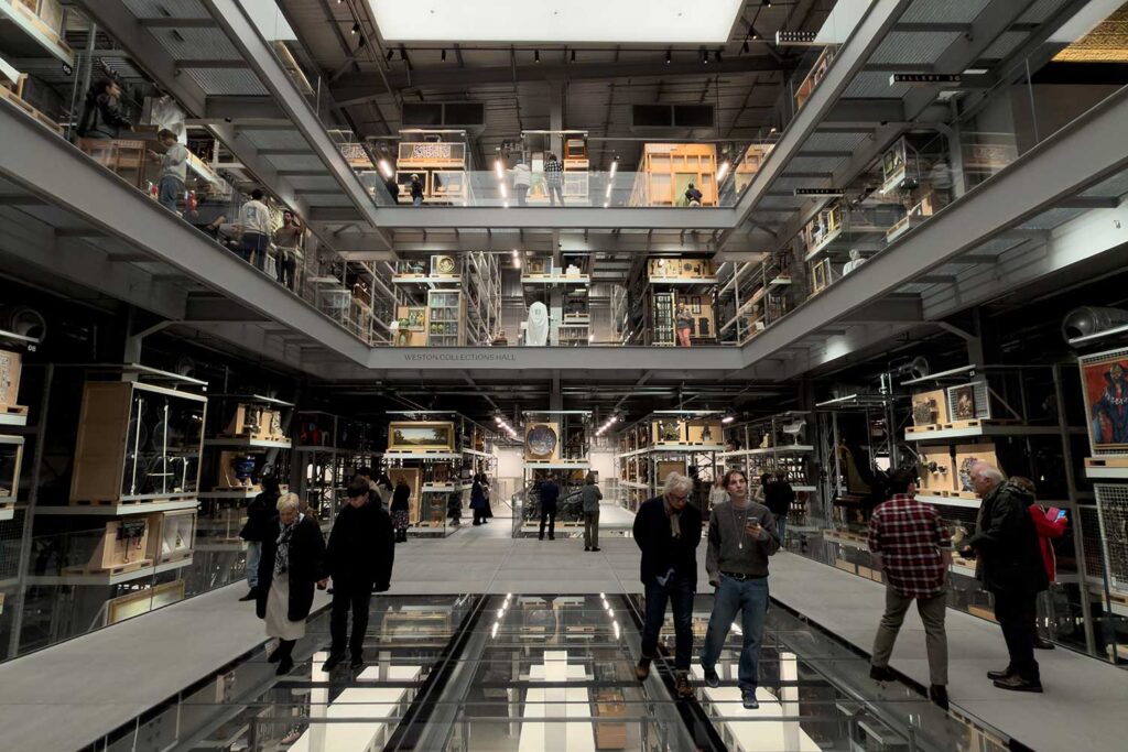A photograph of the interior of the V&A East Storehouse, showing the large central atrium, with its glass floor, and surrounded by shelves of objects.