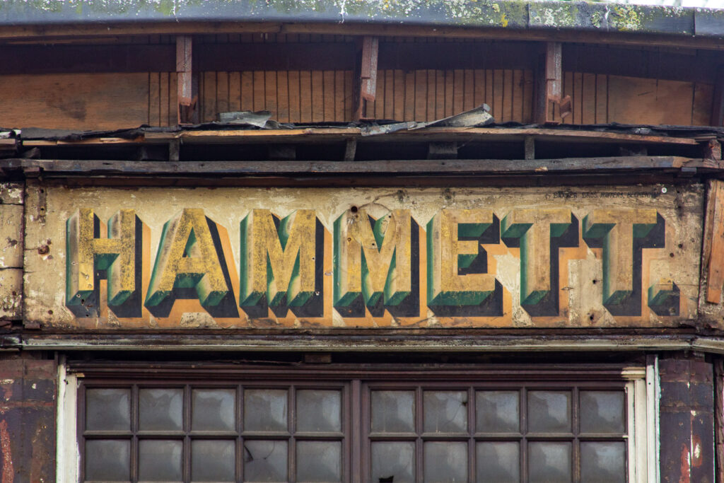 A photograph of a faded shop sign featuring three dimensional lettering for the name HAMMETT.